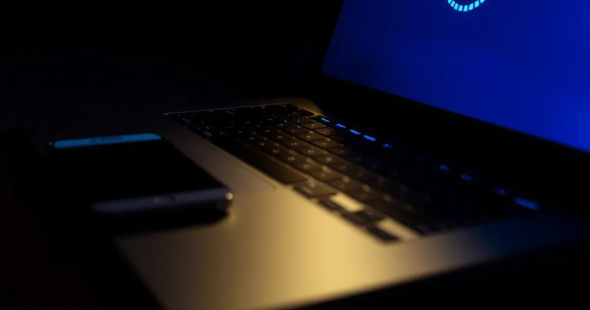 A laptop and phone glowing in a dark room, both showing a payment confirmation still processing, evoking the uncertainty of an unverified crypto payment